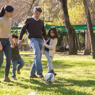 A family plays soccer together in a sunny park, enjoying quality time outdoors.